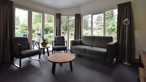 Un salon moderne comprenant un canapé, deux fauteuils, une table basse et de grandes fenêtres donnant sur un paysage verdoyant.