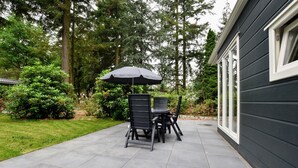 Une terrasse avec une table et des chaises, un parasol, et une maison avec une fenêtre.