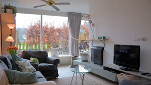 A living room with a sofa, armchair, TV, and a glass coffee table. - Cozy Holiday Home in Noordwijkerhout near Lake (Noordwijkerhout)