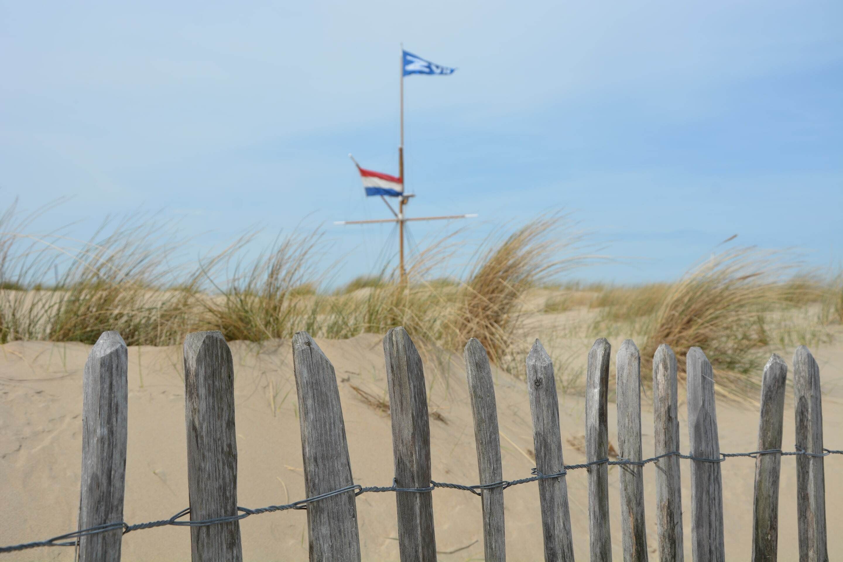 A wooden fence with a flag, sand dunes, and sparse vegetation.