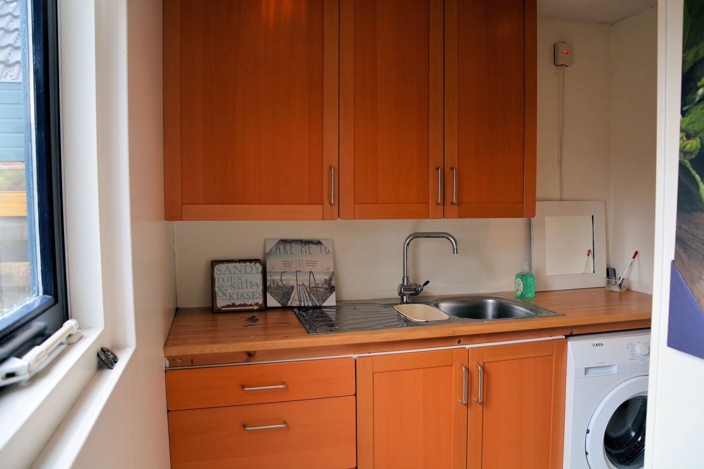 A kitchen with wooden cabinets, a sink, a washing machine, and a window.