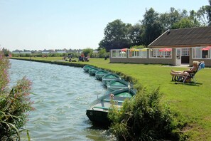 Eine Uferlage mit vertäuten Booten, einer Wiese und einem Gebäude mit Fenstern und Dach.
