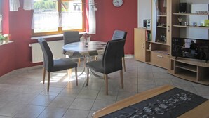 Een eethoek met een ronde tafel, vier stoelen, een klok aan de muur en een boekenkast.