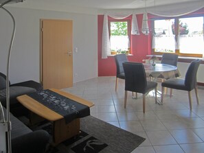 A dining area with a round table and four chairs, a sofa, a small table with a cloth, and a door in the background.