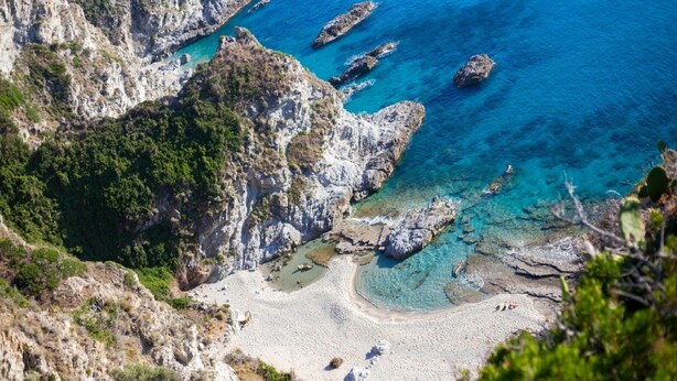 Un paisaje costero con acantilados rocosos, aguas azul cristalino y una playa arenosa.