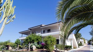 Un edificio de dos pisos con balcones, rodeado de jardines ajardinados y palmeras.