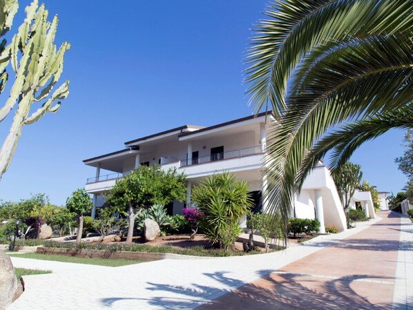 A two-story building with balconies, surrounded by landscaped gardens and palm trees. - Belvilla by OYO Gattotrilo x 4 (Ricadi)