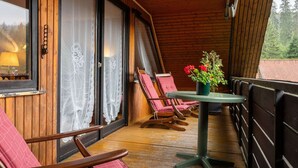 Eine Holzterrasse mit Tisch und Stühlen, einem Blumentopf und Blick auf den Wald.