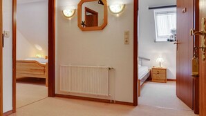 Ein Schlafzimmer mit Holztür, einem weißen Heizkörper, einem Nachttisch mit Lampe und einem Fenster mit Vorhängen.