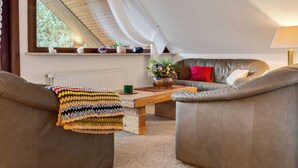 Ein gemütliches Schlafzimmer im Loft-Stil mit schrägem Dach, einem großen Fenster mit Vorhängen, einem Ledersofa, einem kleinen Tisch und einer Heizung.
