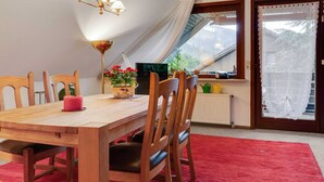 Ein Essbereich mit einem Holztisch, Stühlen, einer Chandelieber, einem Blumentopf mit roten Blüten und Blick auf eine Brücke durch ein Fenster.