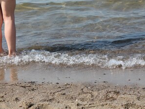 A sandy beach with clear shallow water and a person's legs visible in the water. - Wohnung in Alt Bukow mit Garten (Alt Bukow)