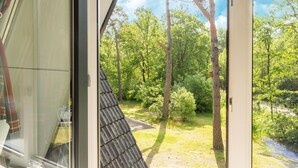 A view from a window of a room with a sloped roof, looking out onto a grassy area with trees and a path.