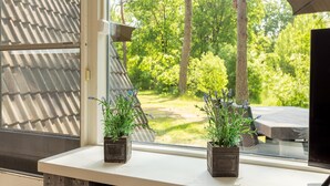 A window with two square planters containing lavender plants, a view of a green garden with trees and a wooden deck.
