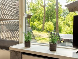Una ventana con dos macetas cuadradas con plantas de lavanda, vista a un jardín verde con árboles y una terraza de madera.