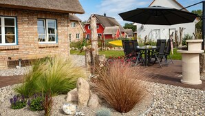 A patio area with a table and chairs, surrounded by a garden with various plants and rocks. - Exklusives Reetdachhaus mit Sauna in Rerik (Rerik)