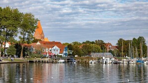 A waterfront scene with a church, boats, and a dock with people. - Exklusives Reetdachhaus mit Sauna in Rerik (Rerik)