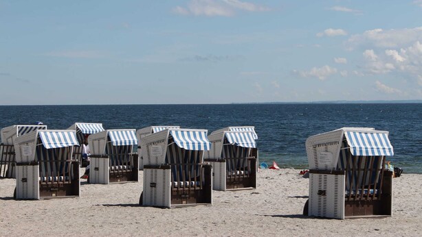 Beach huts with striped awnings, arranged in rows on a sandy beach, overlooking the sea. - Stylish Family Stay by Beach (Boltenhagen)