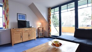 A modern living room with a wooden coffee table, a black sofa, and a television on a wooden cabinet. - Stylish Family Stay by Beach (Boltenhagen)