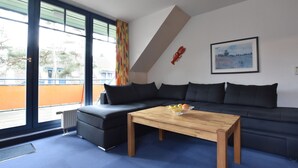 A modern living room with a black sofa, a wooden coffee table, and a large window with curtains. - Stylish Family Stay by Beach (Boltenhagen)