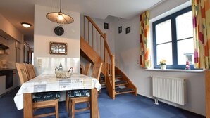 A dining area with a table set for four, wooden chairs, a blue carpet, a wooden staircase, and a window with colorful curtains. - Stylish Family Stay by Beach (Boltenhagen)