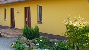 Ein gelbes Gebäude mit einem Ziegeldach, zwei Holztüren und einem kleinen Fenster mit Vorhang.