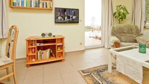 Ein Wohnzimmer mit Bücherregal, Fernseher, Sessel, Couchtisch und einer Pflanze.