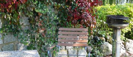 A bench with a metal frame and wooden slats, positioned in front of a stone wall covered with ivy.