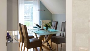 A dining area with a glass table, four chairs, a vase with flowers, and a bottle of wine. - Wohnung in Hoxter Nahe Schloss Corvey (Hoexter)