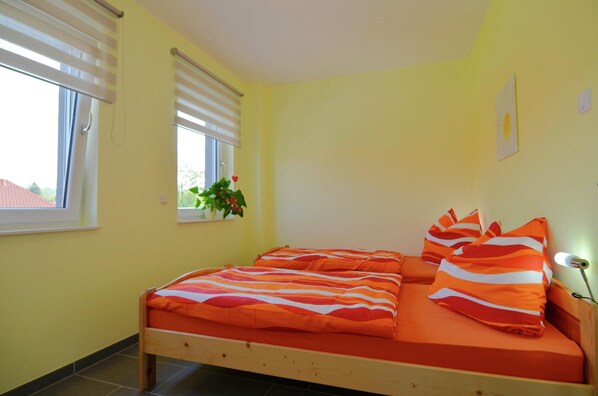 A bedroom with a bed, two windows, and a potted plant.