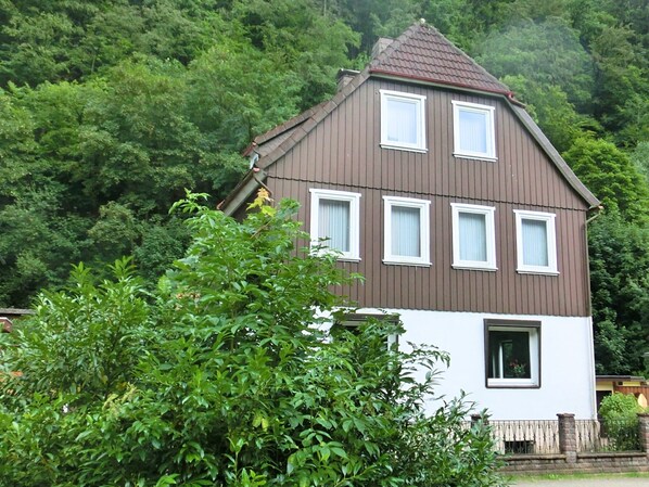 A two-story house with a brown roof and white walls, surrounded by dense green trees. - Geraumiges Haus in Zorge (Walkenried)