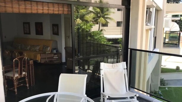 Ein Balkon mit weißen Stühlen und einem Tisch, der auf einen Wohnbereich mit Palmen und einem Gebäude im Hintergrund blickt.