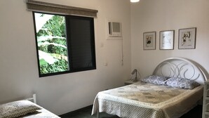 Ein Schlafzimmer mit einem Bett, einem Einzelbett, einem Fenster mit Blick auf Grünflächen und zwei an der Wand befestigten Kunstwerken.