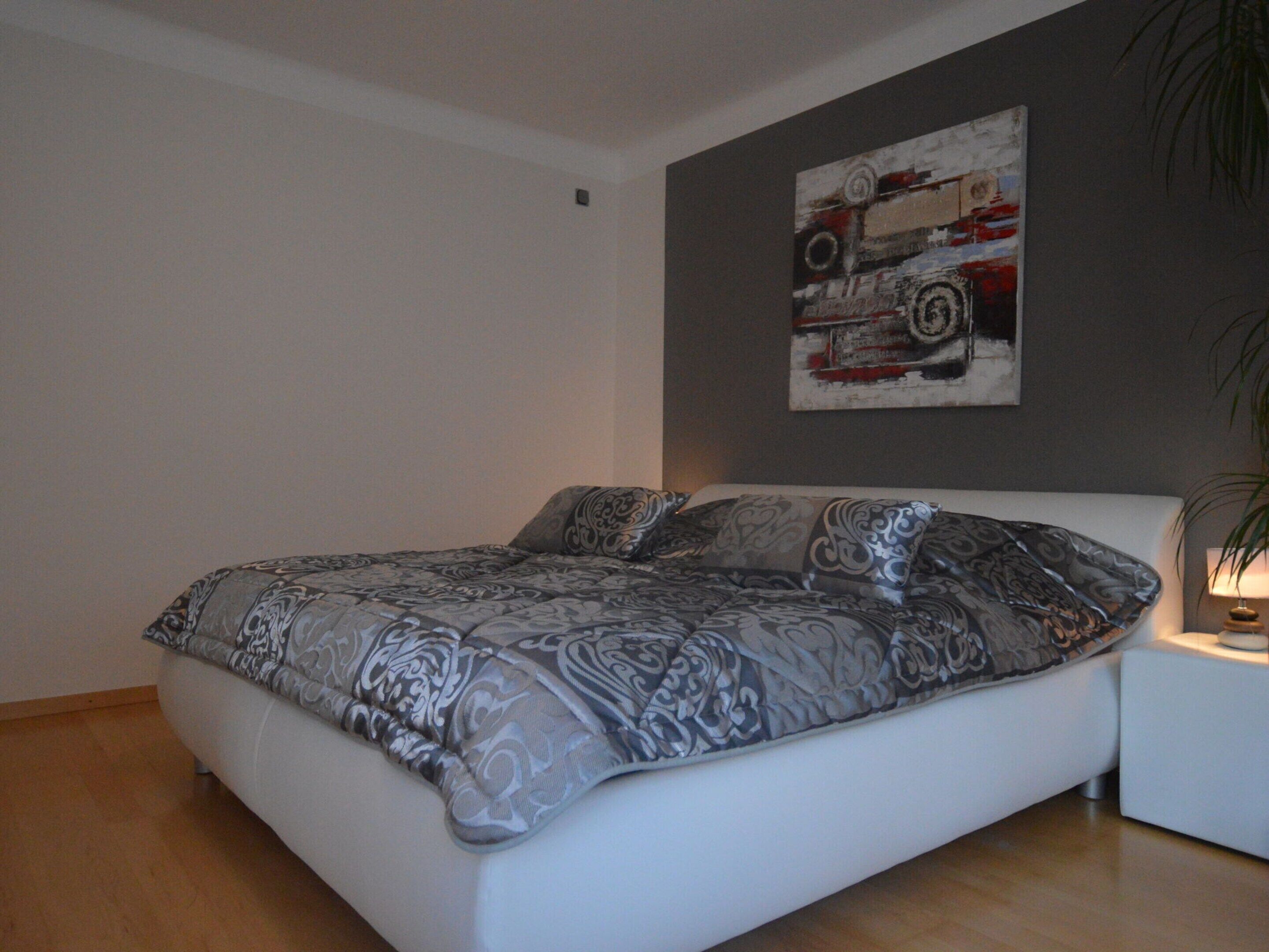 A modern bedroom with a large bed, a white headboard, and a wall-mounted painting.