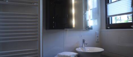 A modern bathroom with a large mirror, a sink, and a window with blinds.