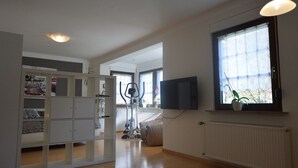 A spacious room with a large window, a flat-screen TV mounted on the wall, and a built-in shelving unit with various items. - Apartment in Trittenheim With Terrace and Garden (Trittenheim)