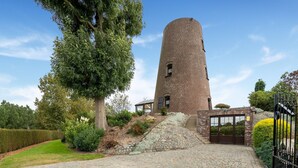 Una torre de ladrillo con una escalera que lleva a una puerta, rodeada de follaje y un camino empedrado.
