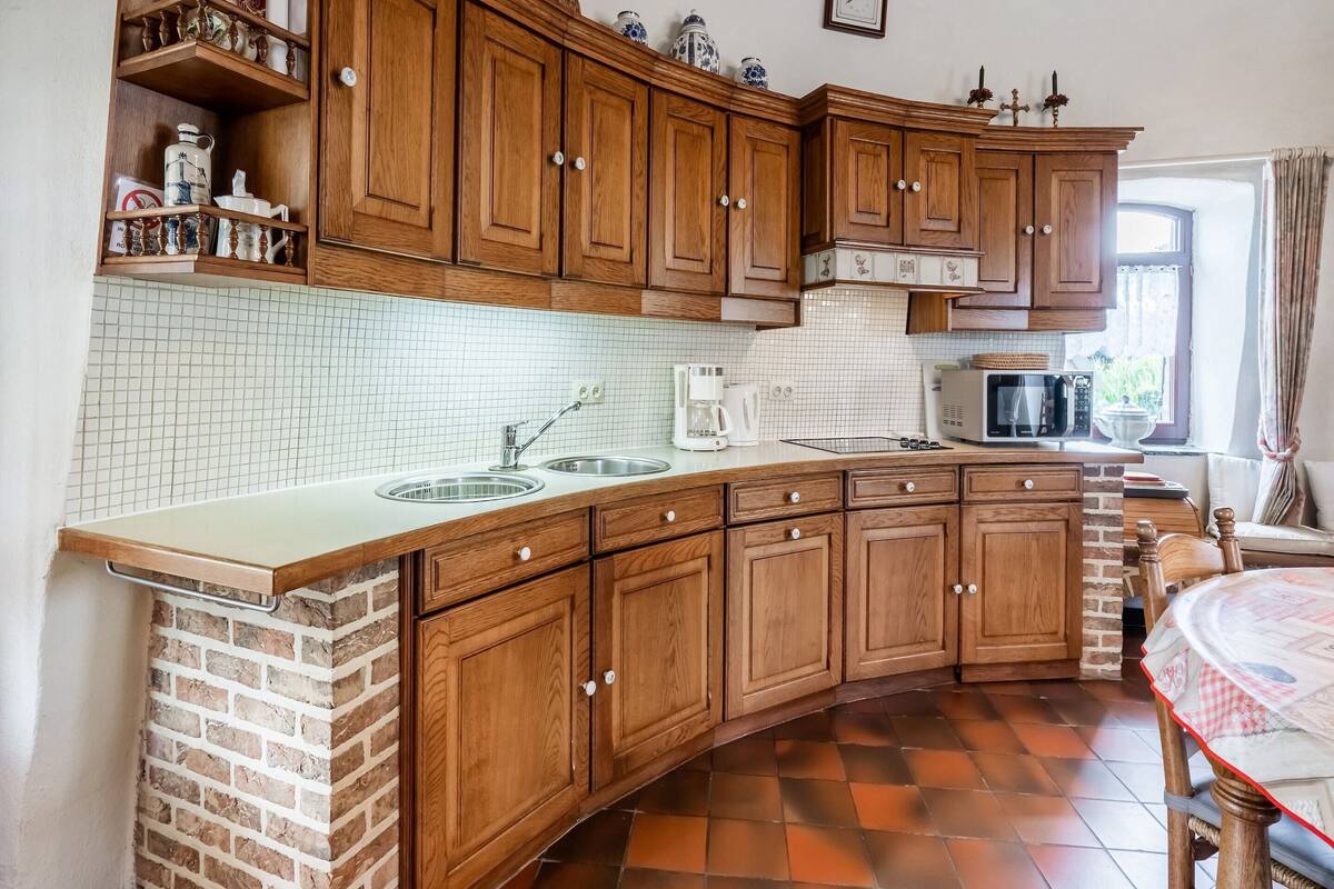 A kitchen with wooden cabinets, a double sink, a microwave, and a brick wall.