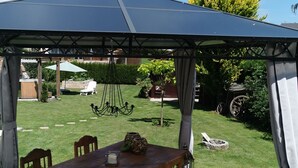A covered patio area with a wooden table and chairs, a hanging light fixture, and a lawn chair in the background. - Wonderful Apartment With Barrel Sauna (Stockheim)