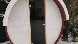 A small, round, white wooden structure with a red trim, featuring a door and a window. - Wonderful Apartment With Barrel Sauna (Stockheim)