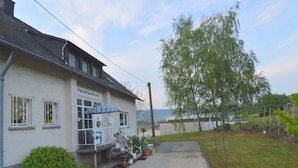 A building labeled "Ferienwohnung" with a paved pathway leading to a covered outdoor seating area. - Cozy Apartment in Neumagen-Dhron near Lake Mosel with Garden (Neumagen-Dhron)