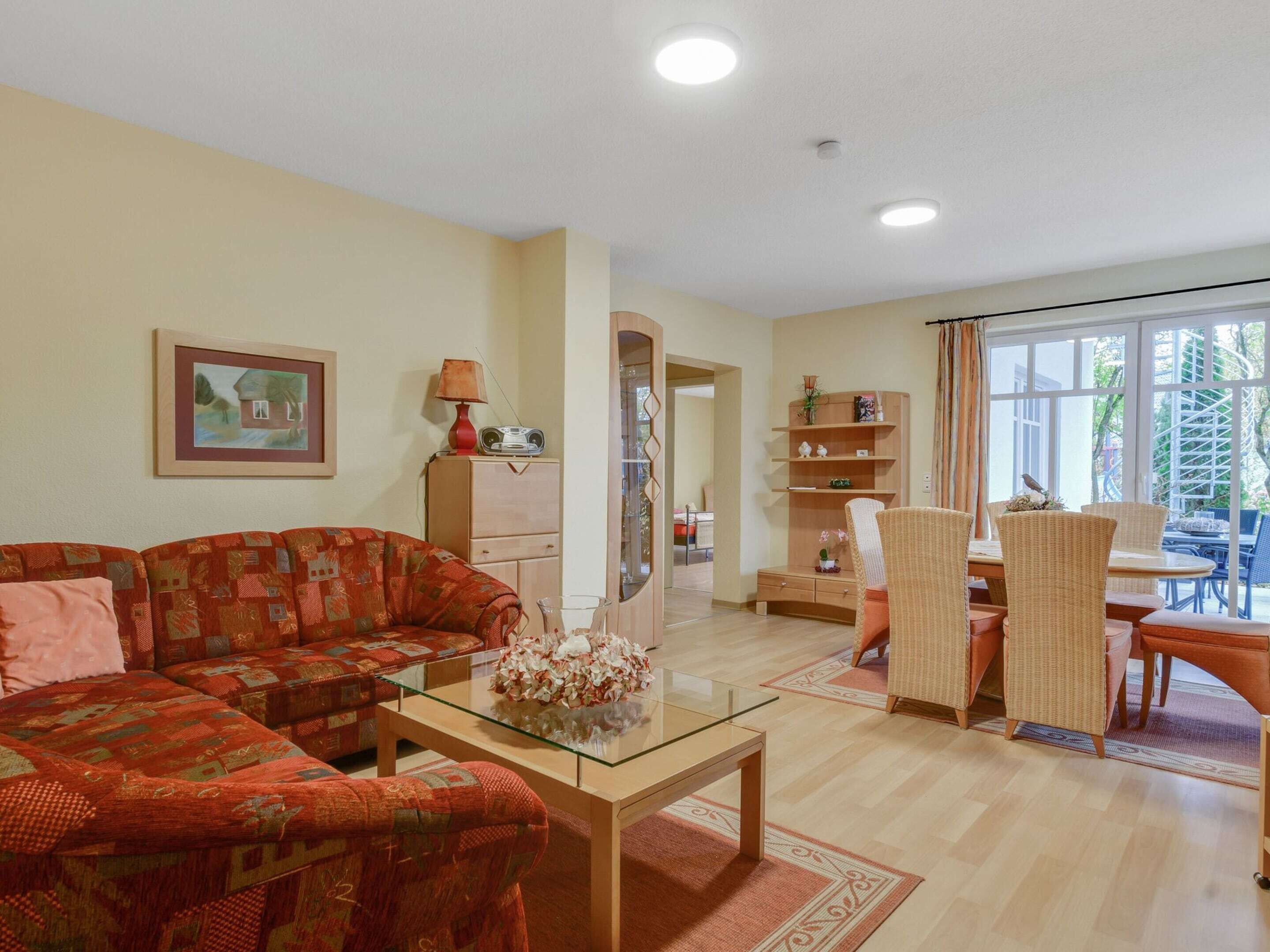 A living room with a sofa, a glass coffee table, and a dining area with wicker chairs and a table.