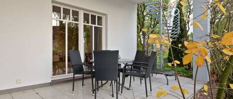 Un patio al aire libre con una mesa y sillas, una zona cubierta con una escalera espiral metálica y vistas a árboles y follaje.