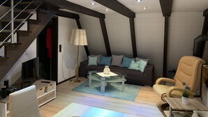 A modern living room with a sofa, armchair, and coffee table. There is a staircase on the left and a door leading to another room. - Pure nature - forest vacation in the Tiny House (Ronshausen)