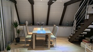 A dining area with a wooden table and chairs, a kitchen in the background, and a staircase. - Pure nature - forest vacation in the Tiny House (Ronshausen)