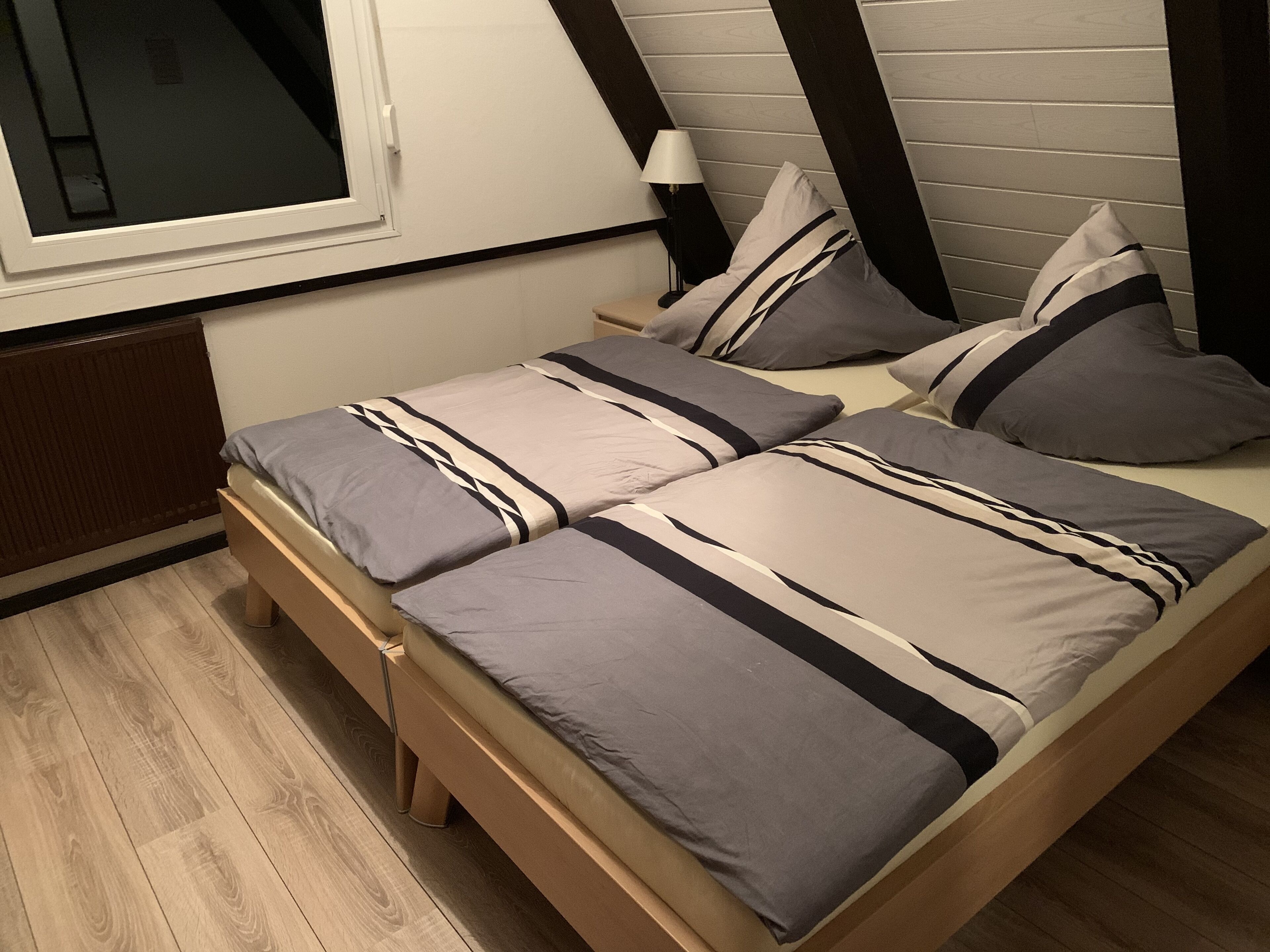 Une petite chambre à coucher, chaleureuse et accueillante, avec un lit simple, une table de chevet, une lampe et une fenêtre.