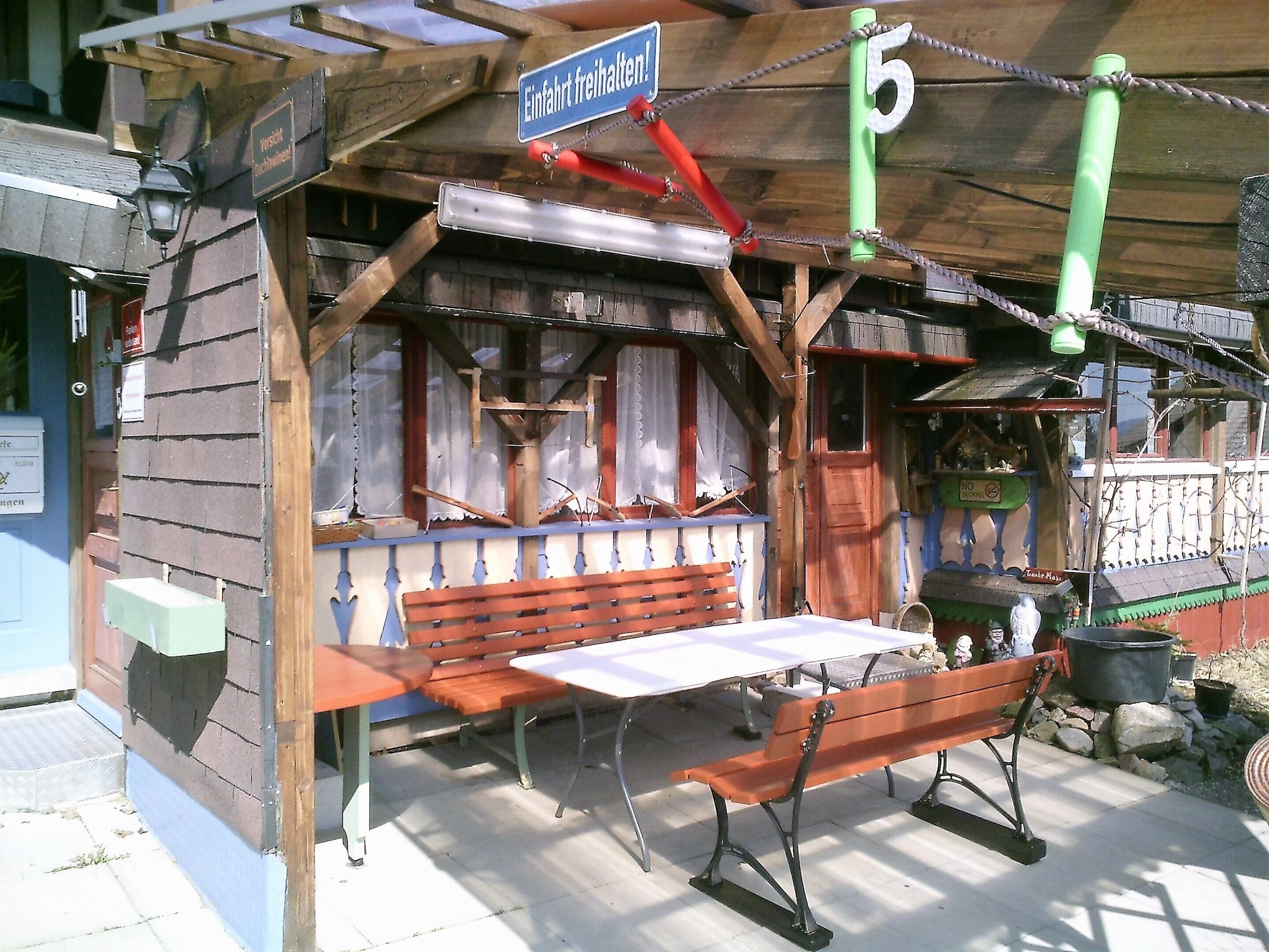 A rustic wooden building with a bench and a table, a sign indicating a free entrance, and a number '5' sign.