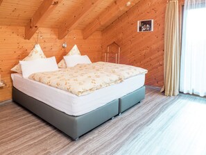 Une pièce aux murs lambrissés, comprenant un lit, une table de chevet, une lampe fixée au mur et une fenêtre avec des rideaux.