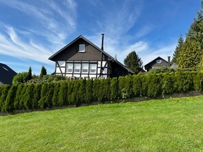 A two-story house with a dark roof and white window frames, surrounded by a well-maintained hedge and a grassy lawn. - Detached Holiday Home in Sauerland near Winterberg with Terrace & Garden (Winterberg)