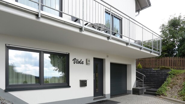 Un bâtiment moderne doté d’un balcon, de grandes fenêtres et d’une plaque signalétique portant le nom « Viola ».